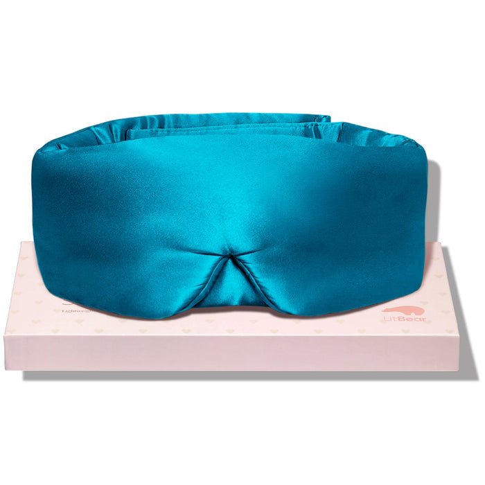 Peacock Blue padded sleep mask with a shaped nose area, resting on a pale pink box.