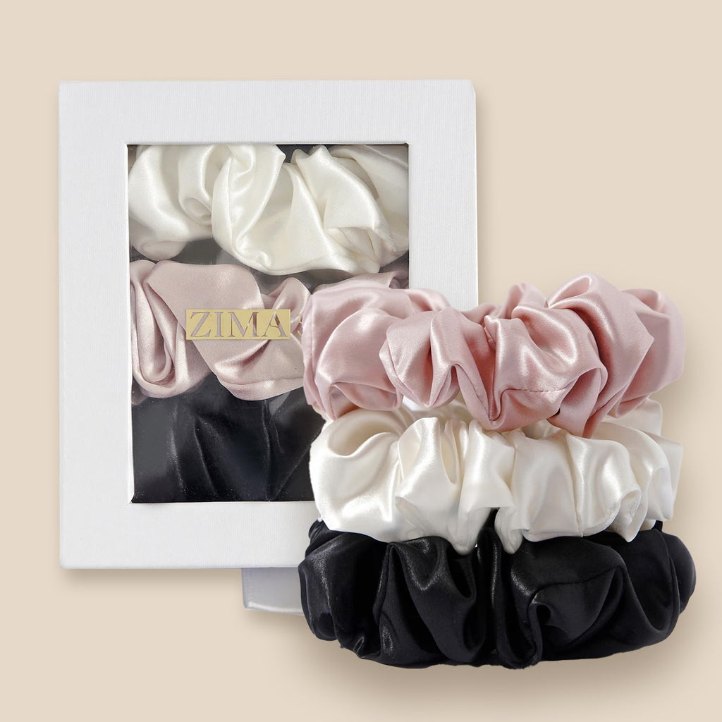 Pink, ivory and black gathered scrunchies stacked in front of a white windowed box with a ZIMA label.