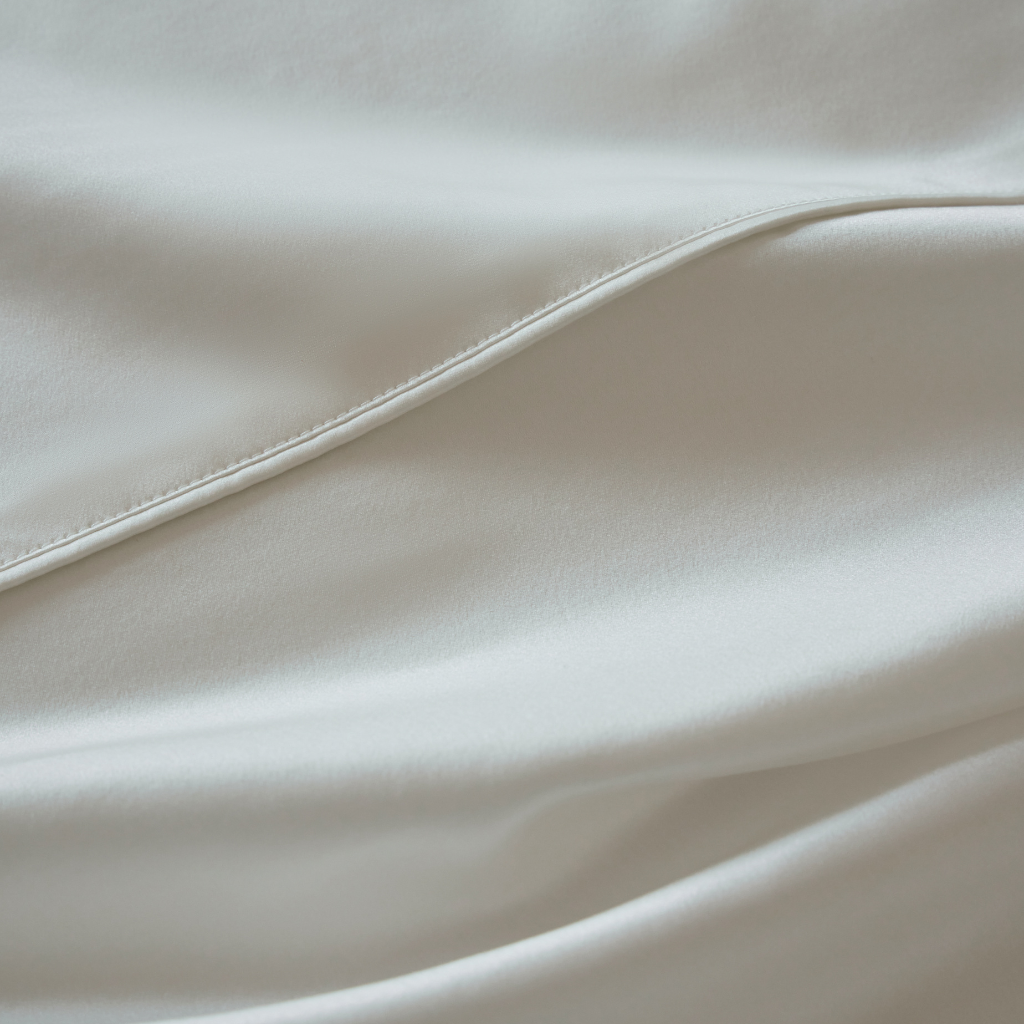 Close-up of Soreia Charmeuse silk flat sheet in Perle light pink, made from 22 Momme pure mulberry silk bedding.