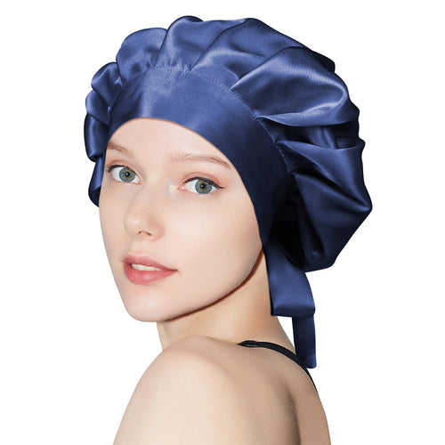 Person wearing a navy gathered sleep bonnet with a wide front band and ties at the back.
